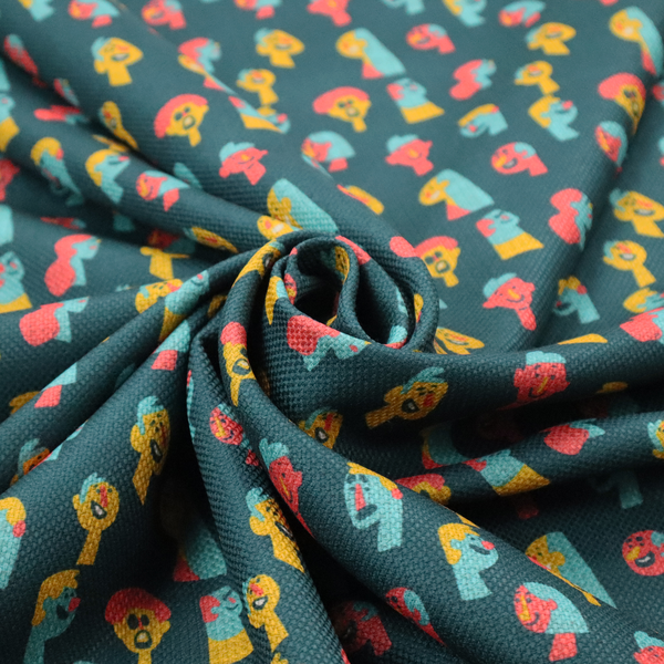 This fabric features a whimsical, repeating pattern on a dark teal background, decorated with stylized, colourful illustrations of diverse human faces in shades of bright yellow, light blue, and coral pink.