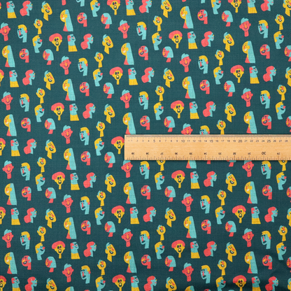 This fabric features a whimsical, repeating pattern on a dark teal background, decorated with stylized, colourful illustrations of diverse human faces in shades of bright yellow, light blue, and coral pink.