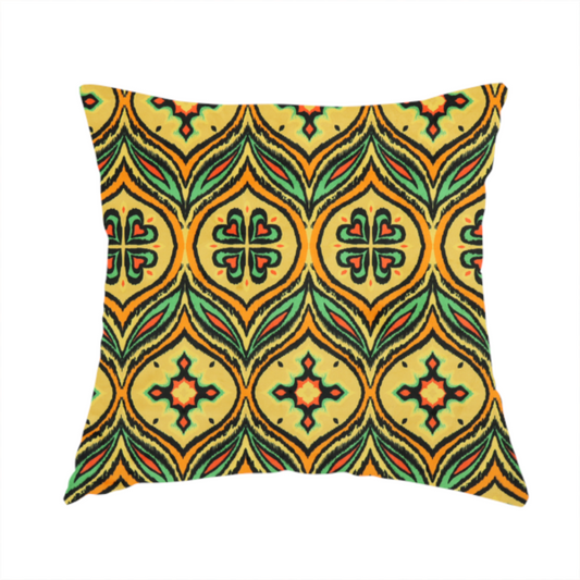 The fabric used to create this handmade cushion is a print featuring a repeating retro ikat ogee pattern. The geometric design displays a lattice of mustard yellow onion arches, green leaf shapes, and four-leaf clover medallions outlined in fuzzy black brushstrokes with pops of coral orange.