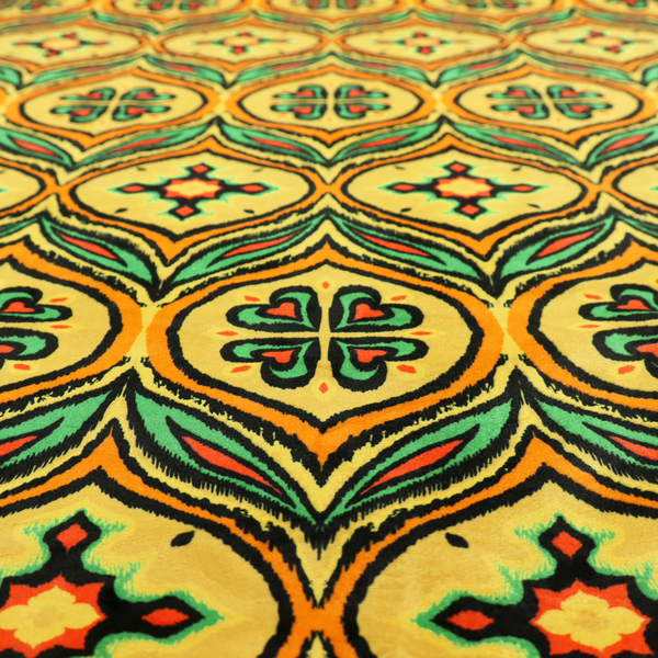 Fabric print featuring a repeating retro ikat ogee pattern. The geometric design displays a lattice of mustard yellow onion arches, green leaf shapes, and four-leaf clover medallions outlined in fuzzy black brushstrokes with pops of coral orange.