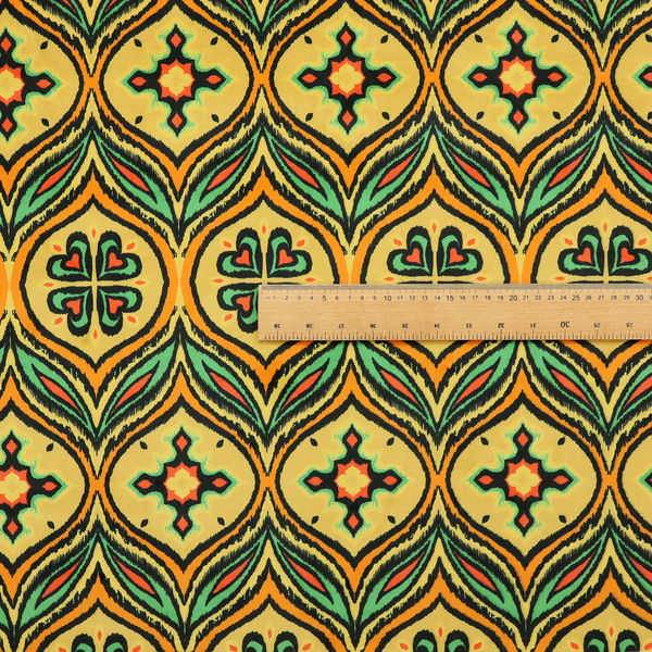 Fabric print featuring a repeating retro ikat ogee pattern. The geometric design displays a lattice of mustard yellow onion arches, green leaf shapes, and four-leaf clover medallions outlined in fuzzy black brushstrokes with pops of coral orange.