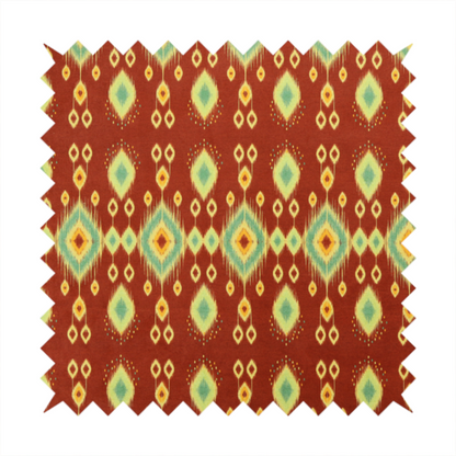 Fabric print featuring a repeating vertical ikat pattern. The design showcases distinct diamond and teardrop motifs with feathered edges in soft sage green, teal, and mustard yellow over a solid terracotta red background.