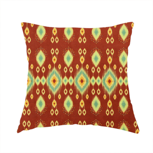 The fabric used to create this handmade cushion is a print featuring a repeating vertical ikat pattern. The design showcases distinct diamond and teardrop motifs with feathered edges in soft sage green, teal, and mustard yellow over a solid terracotta red background.