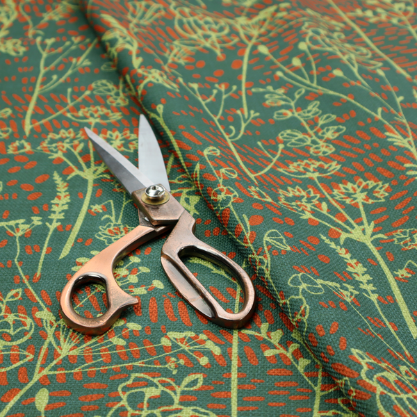 Fabric print featuring a whimsical wildflower meadow pattern. The design showcases delicate lime-green line art sketches of slender stems and blossoms over a deep teal-green background layered with small, textured terracotta orange dashes.