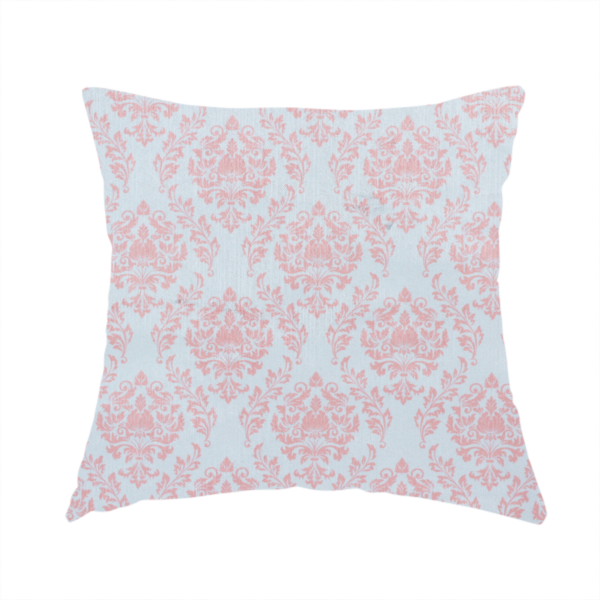 The fabric used to create this handmade cushion is a print featuring a classic, repeating vintage damask pattern. The traditional ornate floral and acanthus leaf motifs are printed in a soft blush pink over a light, pastel icy blue background.
