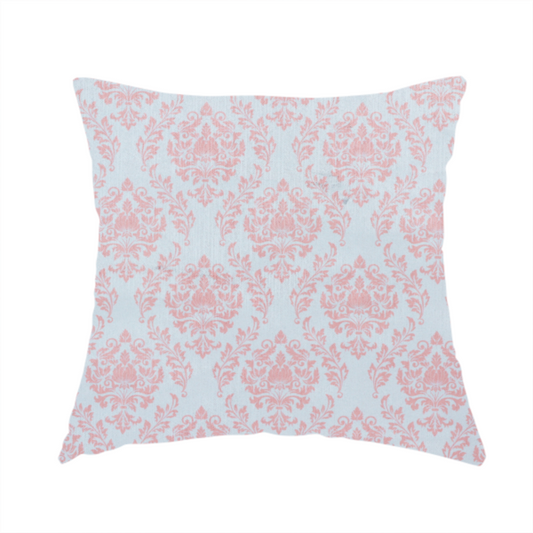 The fabric used to create this handmade cushion is a print featuring a classic, repeating vintage damask pattern. The traditional ornate floral and acanthus leaf motifs are printed in a soft blush pink over a light, pastel icy blue background.