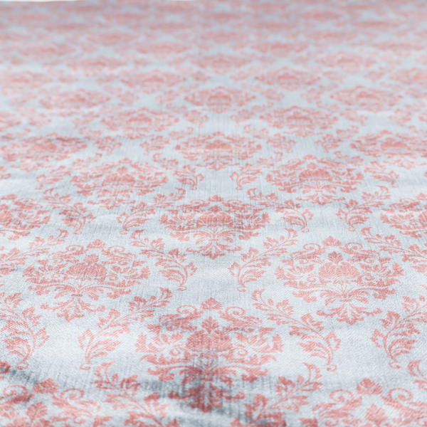 Fabric print featuring a classic, repeating vintage damask pattern. The traditional ornate floral and acanthus leaf motifs are printed in a soft blush pink over a light, pastel icy blue background.