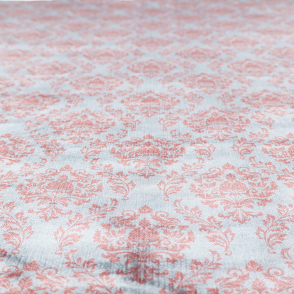Fabric print featuring a classic, repeating vintage damask pattern. The traditional ornate floral and acanthus leaf motifs are printed in a soft blush pink over a light, pastel icy blue background.