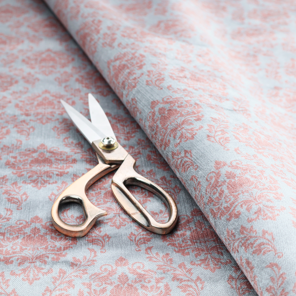Fabric print featuring a classic, repeating vintage damask pattern. The traditional ornate floral and acanthus leaf motifs are printed in a soft blush pink over a light, pastel icy blue background.