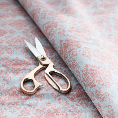 Fabric print featuring a classic, repeating vintage damask pattern. The traditional ornate floral and acanthus leaf motifs are printed in a soft blush pink over a light, pastel icy blue background.