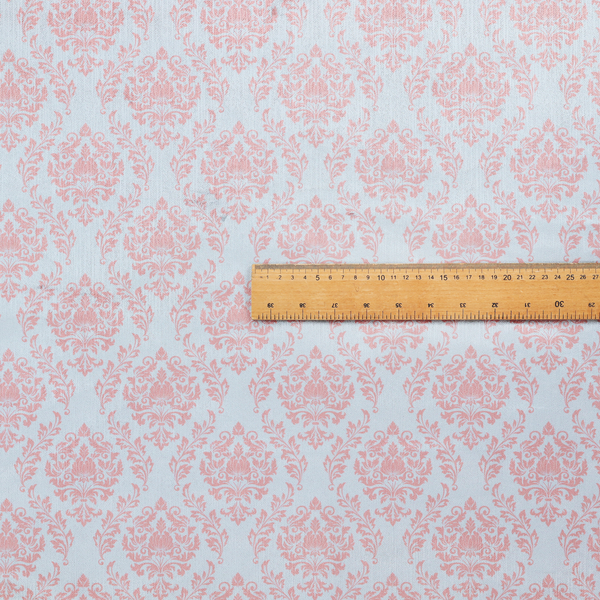 Fabric print featuring a classic, repeating vintage damask pattern. The traditional ornate floral and acanthus leaf motifs are printed in a soft blush pink over a light, pastel icy blue background.