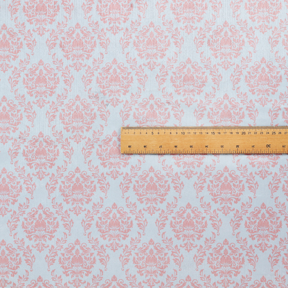 Fabric print featuring a classic, repeating vintage damask pattern. The traditional ornate floral and acanthus leaf motifs are printed in a soft blush pink over a light, pastel icy blue background.