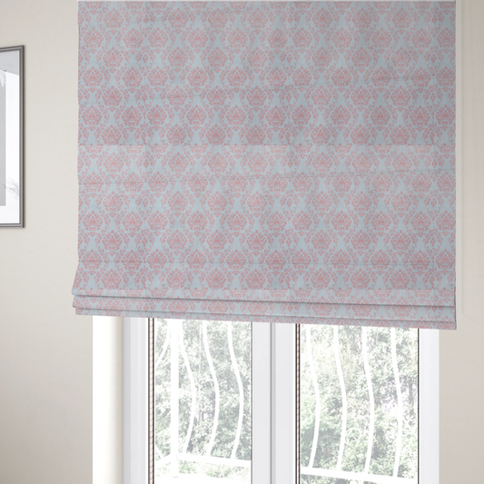 The fabric used to create these Roman blinds is a print featuring a classic, repeating vintage damask pattern. The traditional ornate floral and acanthus leaf motifs are printed in a soft blush pink over a light, pastel icy blue background.