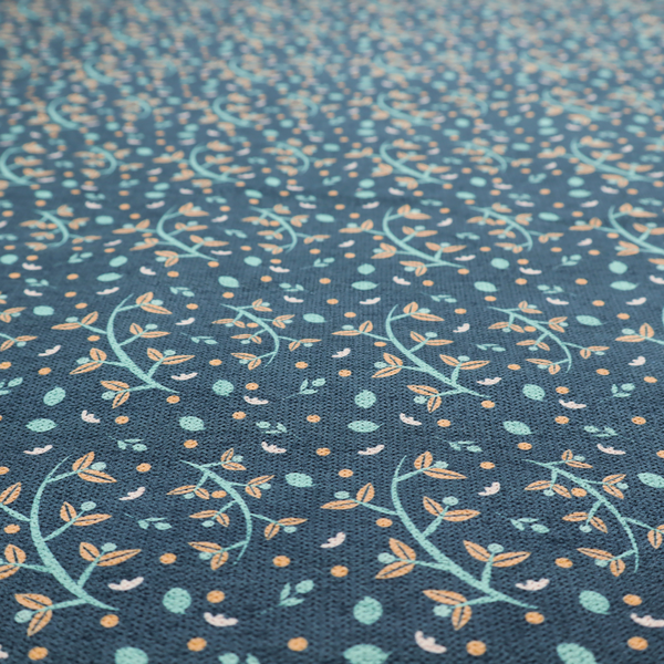 Slate blue textured fabric with a delicate ditsy botanical print. The repeating pattern features thin, curved mint green vine stems with small peach-coloured leaves, surrounded by tiny scattered peach polka dots and miniature teal leaf accents throughout the design.
