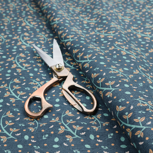 Slate blue textured fabric with a delicate ditsy botanical print. The repeating pattern features thin, curved mint green vine stems with small peach-coloured leaves, surrounded by tiny scattered peach polka dots and miniature teal leaf accents throughout the design.