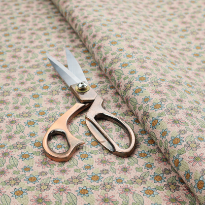 Textured dusty blush pink fabric with a dense retro calico print. The intricate pattern features small, sketch-style daisies with mustard yellow centres and blue-teal petals, mixed with pink blooms and delicate sage green leaves spread tightly across the surface.
