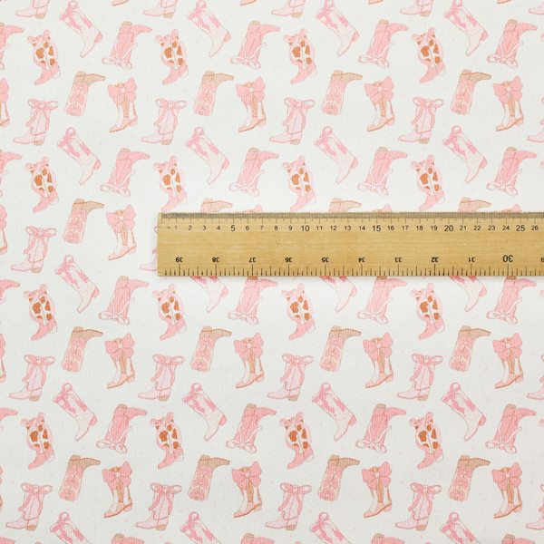 A repeating seamless pattern featuring an assortment of illustrated cowboy and cowgirl boots against a clean, off-white background. The boots are rendered in a soft, whimsical style with a colour palette consisting of various shades of pink, cream, light tan, and occasional brown accents.