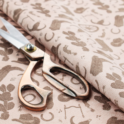 A repeating toile-style western pattern featuring classic cowboy motifs printed in a monochromatic, textured medium-brown hue against a light beige background.