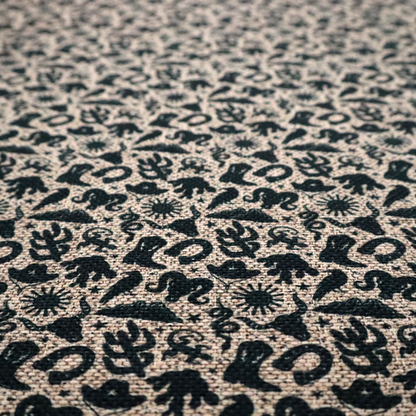 A dense, repeating pattern featuring black graphic silhouettes of classic southwestern and western elements printed on a heavily textured, woven beige fabric base.