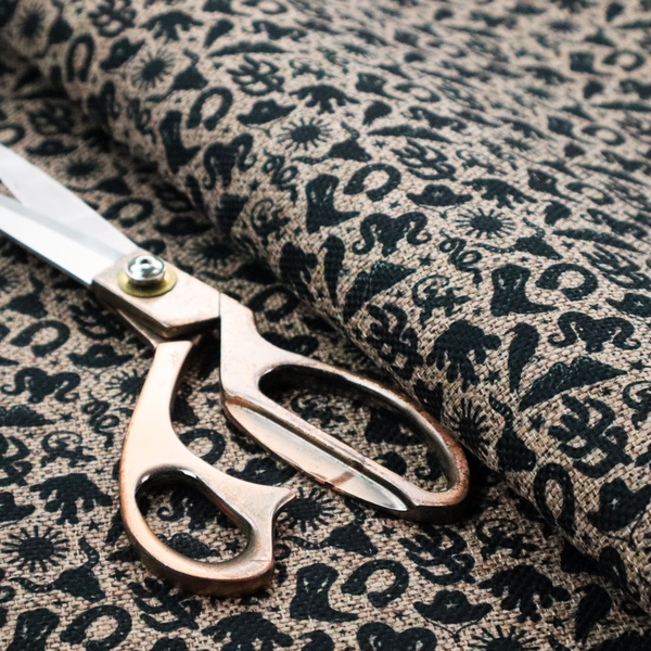 A dense, repeating pattern featuring black graphic silhouettes of classic southwestern and western elements printed on a heavily textured, woven beige fabric base.