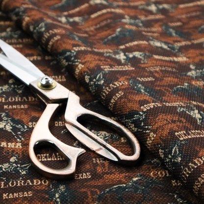 A dark, moody, repeating western tapestry pattern featuring realistic, vintage-style illustrations of cowboys on horseback, set against a deeply textured dark brown background. The palette relies on rich chocolate brown, earthy terracotta tones, and contrast details in cream and muted slate blue.