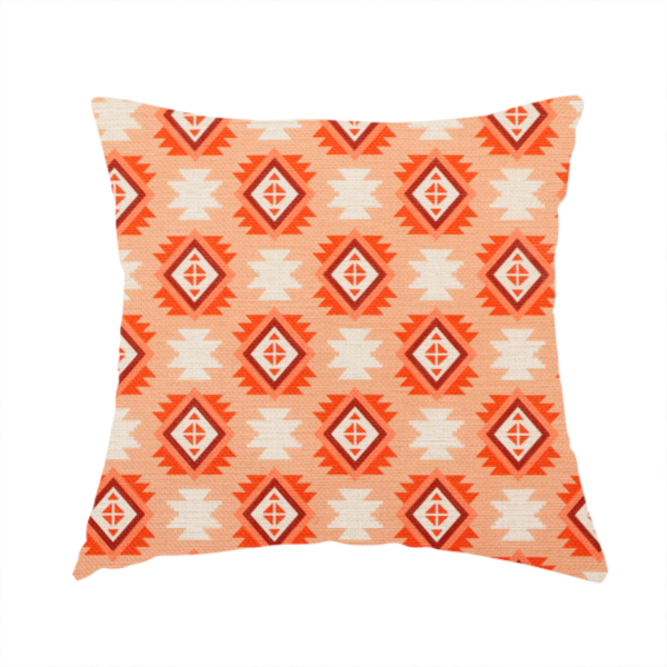 The fabric used to create this handmade cushion is a uniform, repeating geometric pattern featuring southwestern and tribal-inspired motifs printed on a linen-textured background. The colour palette relies on warm, sun-baked tones, including a soft peach backdrop, vibrant terracotta orange, rust brown, and cream accents.