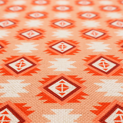 A uniform, repeating geometric pattern featuring southwestern and tribal-inspired motifs printed on a linen-textured background. The colour palette relies on warm, sun-baked tones, including a soft peach backdrop, vibrant terracotta orange, rust brown, and cream accents.