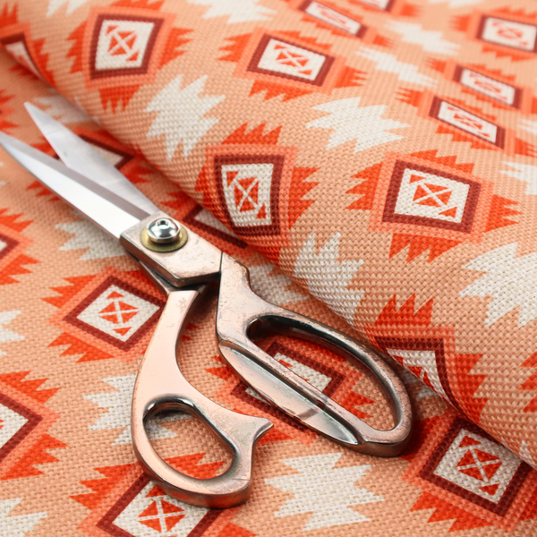 A uniform, repeating geometric pattern featuring southwestern and tribal-inspired motifs printed on a linen-textured background. The colour palette relies on warm, sun-baked tones, including a soft peach backdrop, vibrant terracotta orange, rust brown, and cream accents.