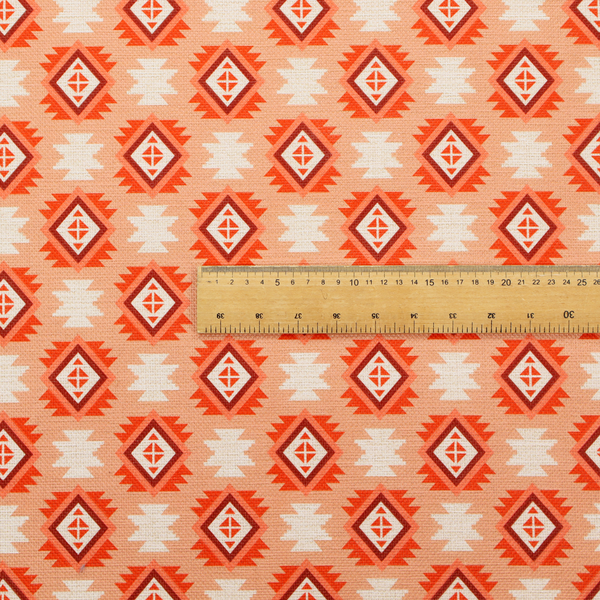 A uniform, repeating geometric pattern featuring southwestern and tribal-inspired motifs printed on a linen-textured background. The colour palette relies on warm, sun-baked tones, including a soft peach backdrop, vibrant terracotta orange, rust brown, and cream accents.