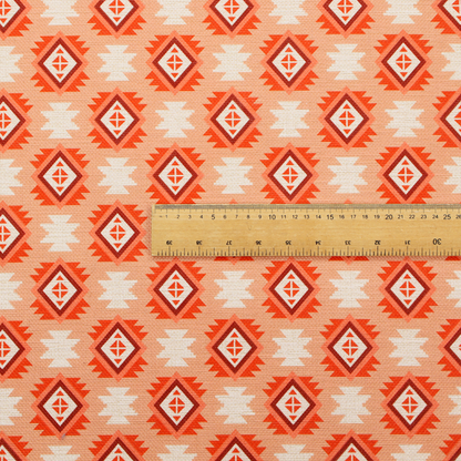 A uniform, repeating geometric pattern featuring southwestern and tribal-inspired motifs printed on a linen-textured background. The colour palette relies on warm, sun-baked tones, including a soft peach backdrop, vibrant terracotta orange, rust brown, and cream accents.