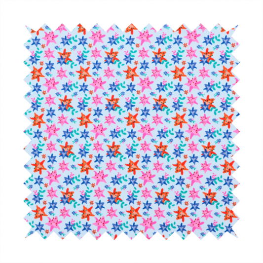 A dense, small-scale tropical ditsy pattern. The design consists of repeating star-shaped lily blossoms in bright shades of orange, magenta pink, and medium blue, accented with tiny teal green leafy sprigs and miniature blue flowers, all distributed across a solid light sky-blue background.