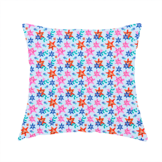 The fabric used to create this handmade cushion is a dense, small-scale tropical ditsy pattern. The design consists of repeating star-shaped lily blossoms in bright shades of orange, magenta pink, and medium blue, accented with tiny teal green leafy sprigs and miniature blue flowers, all distributed across a solid light sky-blue background.