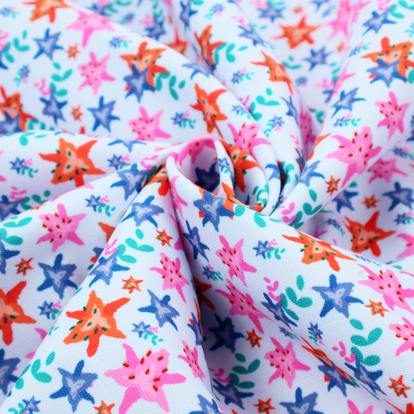 A dense, small-scale tropical ditsy pattern. The design consists of repeating star-shaped lily blossoms in bright shades of orange, magenta pink, and medium blue, accented with tiny teal green leafy sprigs and miniature blue flowers, all distributed across a solid light sky-blue background.