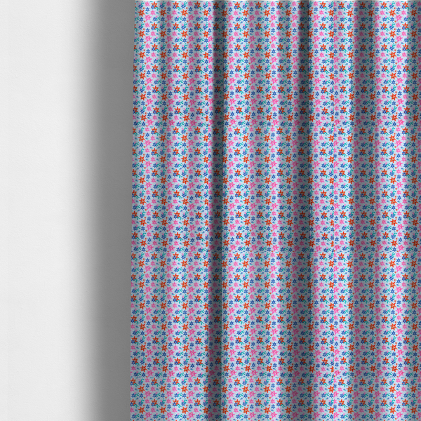 The fabric used to create these made-to-measure curtains is a dense, small-scale tropical ditsy pattern. The design consists of repeating star-shaped lily blossoms in bright shades of orange, magenta pink, and medium blue, accented with tiny teal green leafy sprigs and miniature blue flowers, all distributed across a solid light sky-blue background.