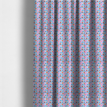 The fabric used to create these made-to-measure curtains is a dense, small-scale tropical ditsy pattern. The design consists of repeating star-shaped lily blossoms in bright shades of orange, magenta pink, and medium blue, accented with tiny teal green leafy sprigs and miniature blue flowers, all distributed across a solid light sky-blue background.