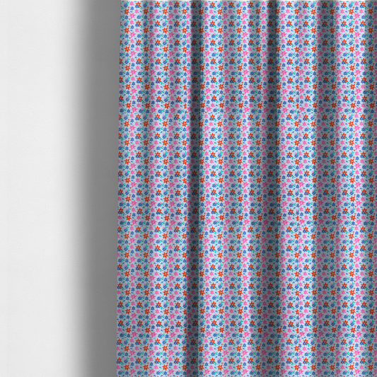 The fabric used to create these made-to-measure curtains is a dense, small-scale tropical ditsy pattern. The design consists of repeating star-shaped lily blossoms in bright shades of orange, magenta pink, and medium blue, accented with tiny teal green leafy sprigs and miniature blue flowers, all distributed across a solid light sky-blue background.