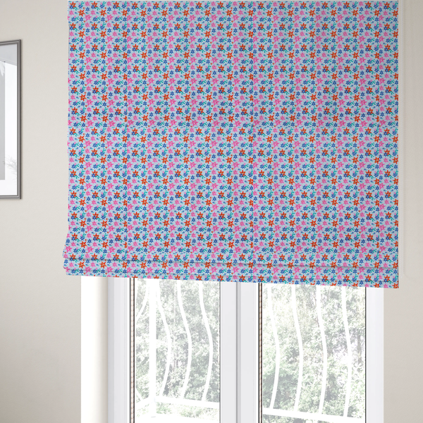 The fabric used to create these Roman blinds is a dense, small-scale tropical ditsy pattern. The design consists of repeating star-shaped lily blossoms in bright shades of orange, magenta pink, and medium blue, accented with tiny teal green leafy sprigs and miniature blue flowers, all distributed across a solid light sky-blue background.