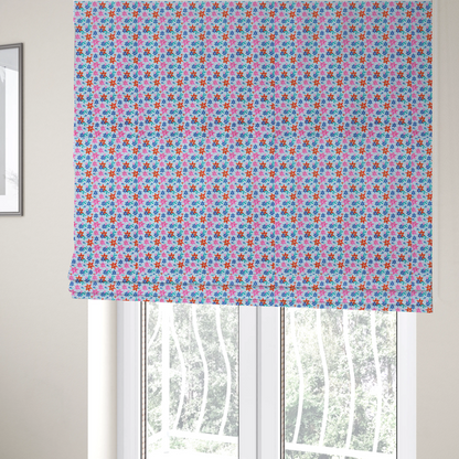 The fabric used to create these Roman blinds is a dense, small-scale tropical ditsy pattern. The design consists of repeating star-shaped lily blossoms in bright shades of orange, magenta pink, and medium blue, accented with tiny teal green leafy sprigs and miniature blue flowers, all distributed across a solid light sky-blue background.