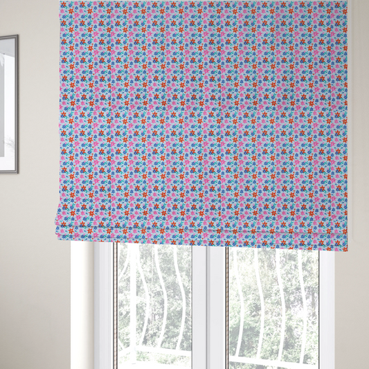 The fabric used to create these Roman blinds is a dense, small-scale tropical ditsy pattern. The design consists of repeating star-shaped lily blossoms in bright shades of orange, magenta pink, and medium blue, accented with tiny teal green leafy sprigs and miniature blue flowers, all distributed across a solid light sky-blue background.