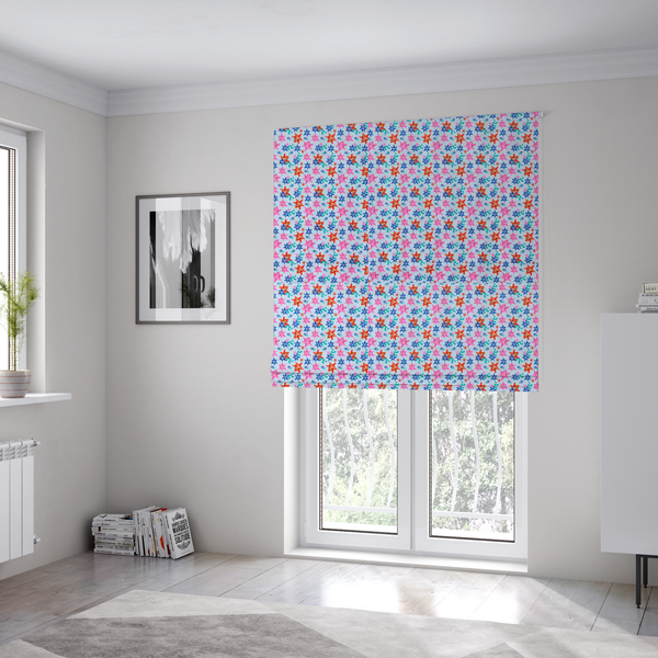 The fabric used to create these Roman blinds is a dense, small-scale tropical ditsy pattern. The design consists of repeating star-shaped lily blossoms in bright shades of orange, magenta pink, and medium blue, accented with tiny teal green leafy sprigs and miniature blue flowers, all distributed across a solid light sky-blue background.