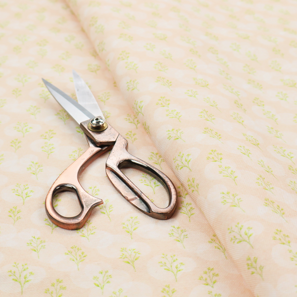A soft watercolour design. The background consists of a subtle pastel peach wash layered with faint, painterly off-white circular polka dots. Arranged in neat diagonal rows over the circles are miniature, light lime green botanical sprigs and fine leaf stems.