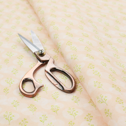 A soft watercolour design. The background consists of a subtle pastel peach wash layered with faint, painterly off-white circular polka dots. Arranged in neat diagonal rows over the circles are miniature, light lime green botanical sprigs and fine leaf stems.