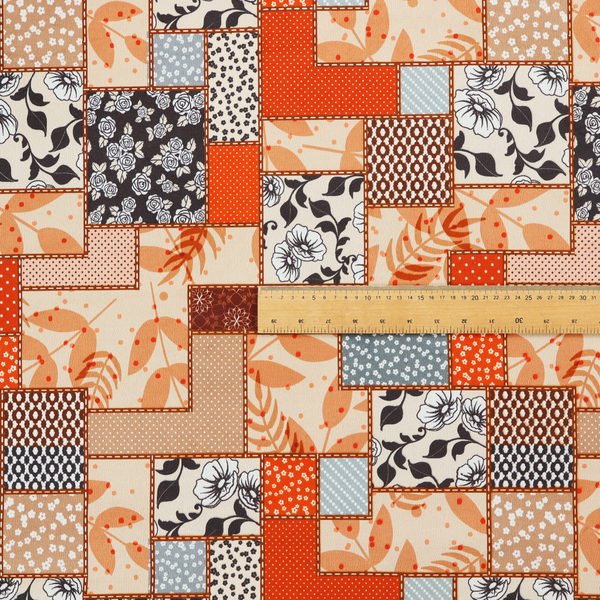 A patchwork fabric pattern featuring a mix of rectangular blocks with floral prints, polka dots, autumn leaves, and geometric shapes in orange, beige, brown, and black-and-white.