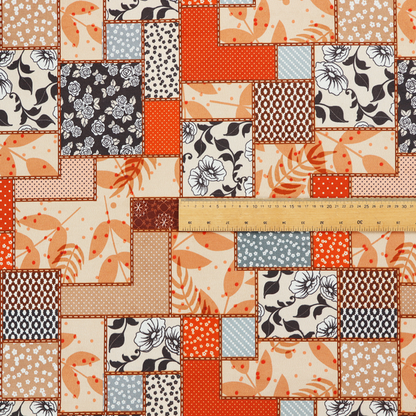 A patchwork fabric pattern featuring a mix of rectangular blocks with floral prints, polka dots, autumn leaves, and geometric shapes in orange, beige, brown, and black-and-white.