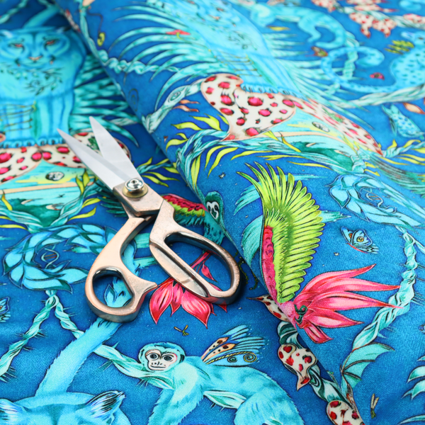 A vibrant turquoise blue fabric featuring an intricate, symmetrical maximalist print of a mythical tropical rainforest. Large, ethereal blue tigers with pink accents are flanked by dense fronds. The repeating pattern is filled with exotic jungle wildlife, including leopards, sloths hanging from vines, winged monkeys, bats, and colourful macaws in shades of bright pink and lime green.