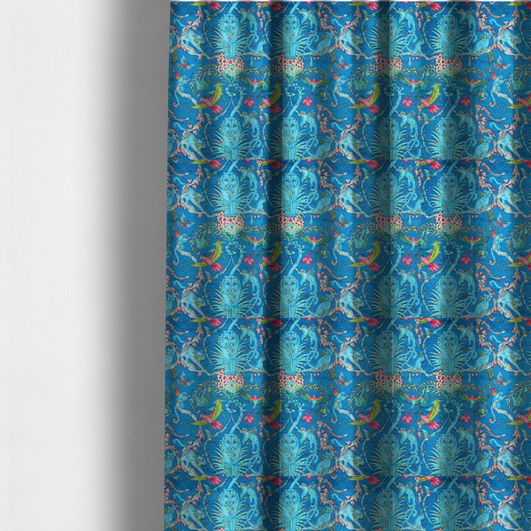 The fabric used to create these made-to-measure curtains is a vibrant turquoise blue fabric featuring an intricate, symmetrical maximalist print of a mythical tropical rainforest. Large, ethereal blue tigers with pink accents are flanked by dense fronds. The repeating pattern is filled with exotic jungle wildlife, including leopards, sloths hanging from vines, winged monkeys, bats, and colourful macaws in shades of bright pink and lime green.