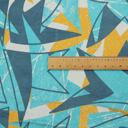 Fabric featuring a bold, retro geometric pattern with abstract, sharp arrow and shard shapes in turquoise, slate blue, mustard yellow, and white with a distressed texture.