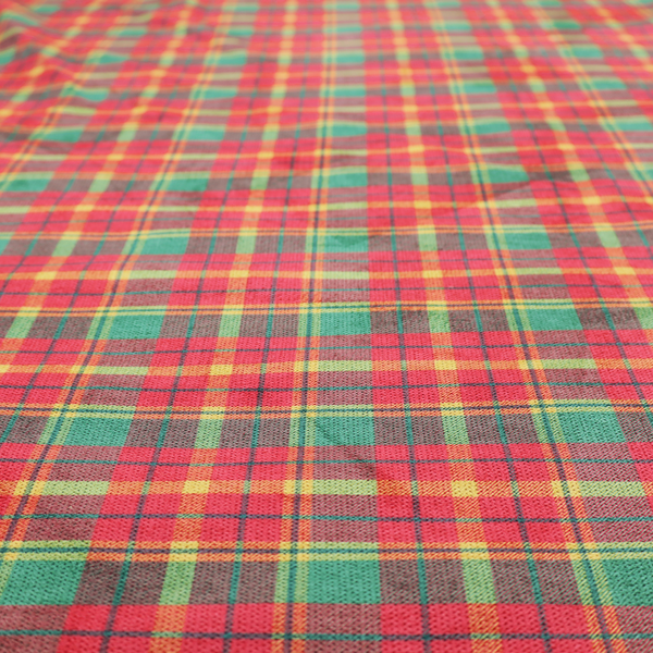 A warm red and green plaid fabric pattern featuring a dense grid of intersecting yellow, dark green, and thin blue stripes.