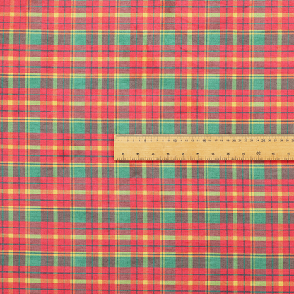 A warm red and green plaid fabric pattern featuring a dense grid of intersecting yellow, dark green, and thin blue stripes.