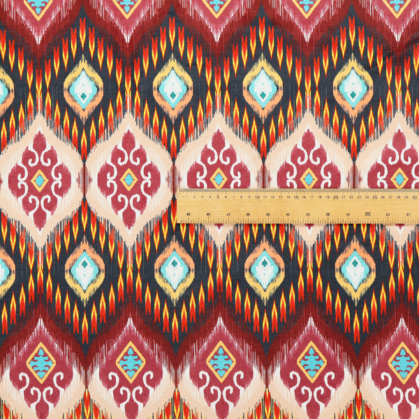 A vibrant, ornate ikat fabric pattern featuring rows of decorative diamond emblems, flame-like borders, and intricate scrollwork motifs in red, black, beige, and turquoise.